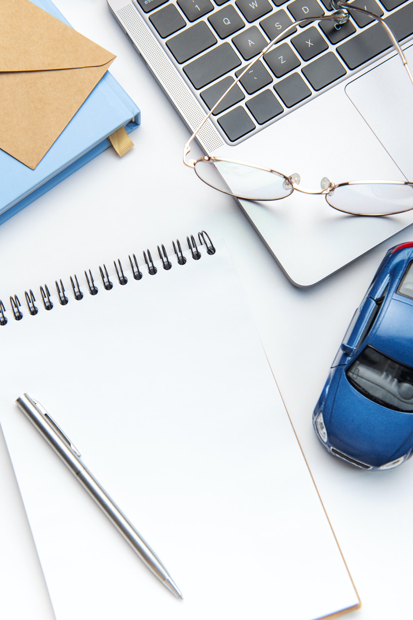 Modern white office desk table with laptop, notebook, toy car and other supplies.